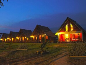 A row of thatched-roof cottages with a well-lit main building. - Best Life Eco Resort Mattala (Hambantota)