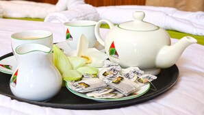 Un plateau avec une théière, des tasses, un pichet et des sachets de thé, posé sur un lit recouvert de draps blancs et doté d’une tête de lit en bois.