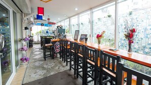 A restaurant with a long wooden counter, black chairs, and large windows. - Nittaya Residence (Bangkok)