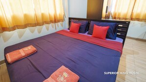 A bed with a purple and red bedspread, two red pillows, and a folded orange towel on the side. - Nittaya Residence (Bangkok)