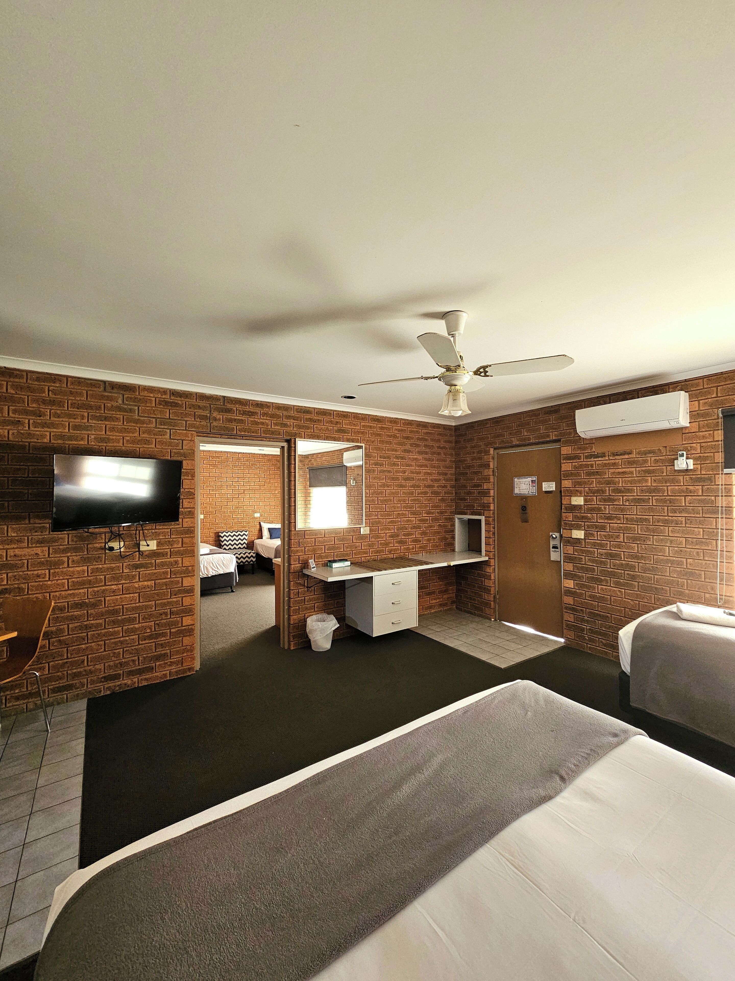 Hotelkamer met bakstenen muren, een flatscreen televisie, een bureau met lades, een bed, een plafondventilator en een airconditioning.