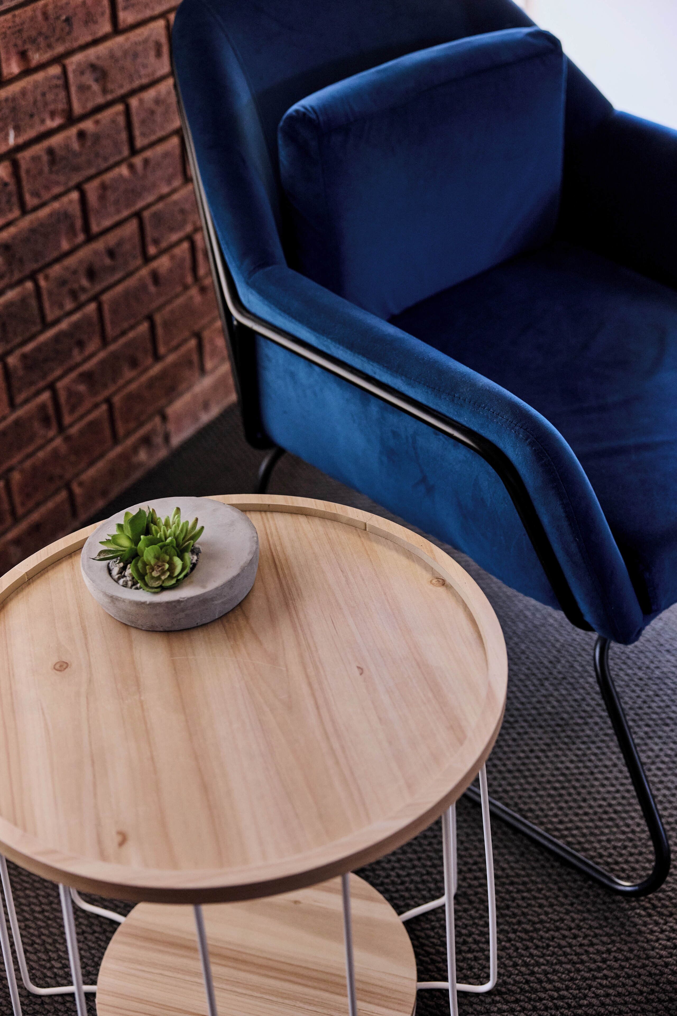 Une chaise bleue, une table ronde en bois et une petite plante en pot.
