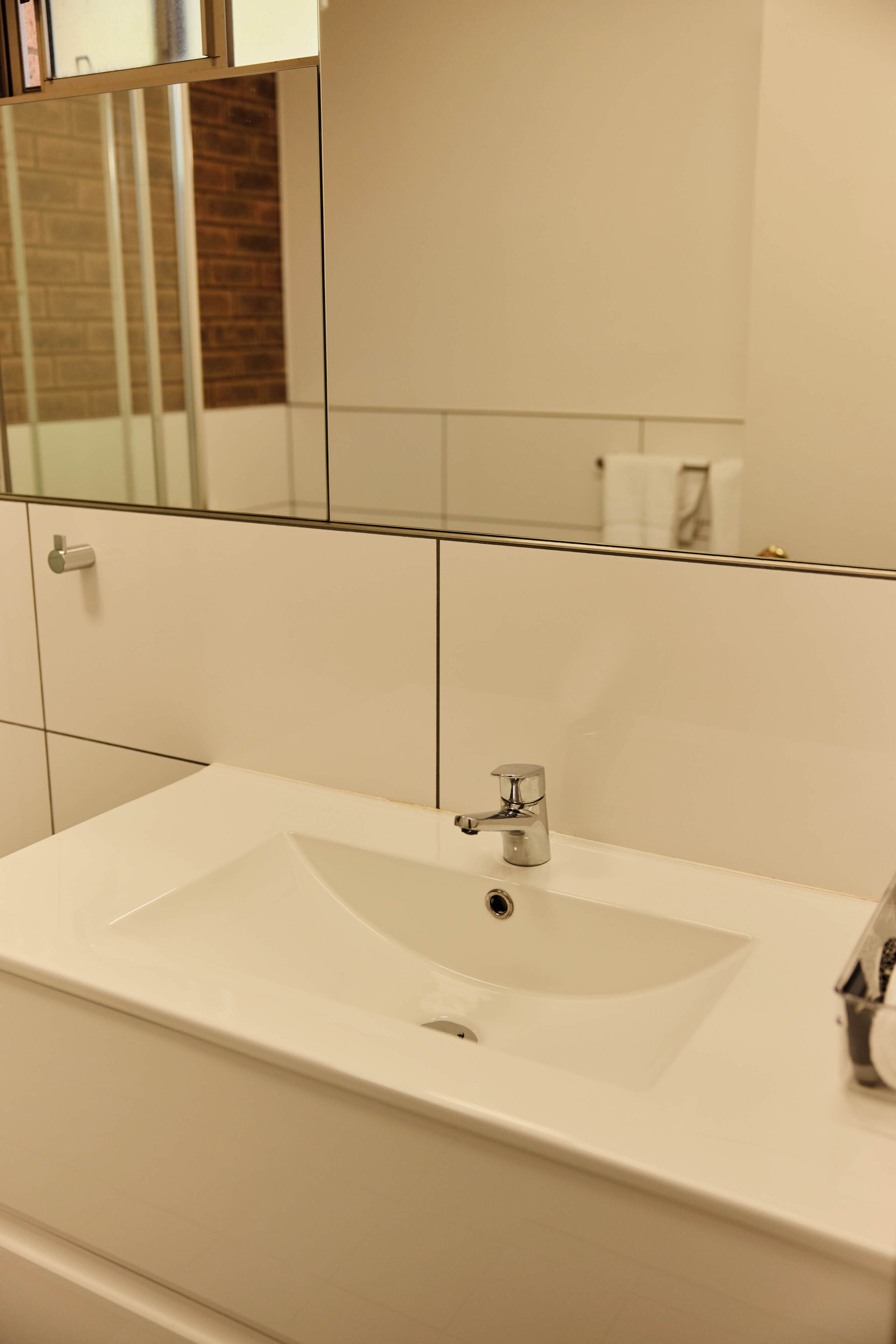 Un baño con un lavabo blanco, un espejo y un muro cubierto de azulejos.