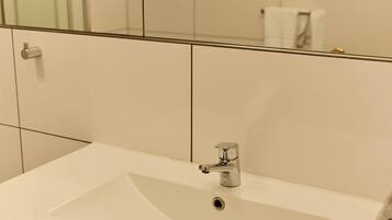 Un baño con un lavabo blanco, un espejo y un muro cubierto de azulejos.