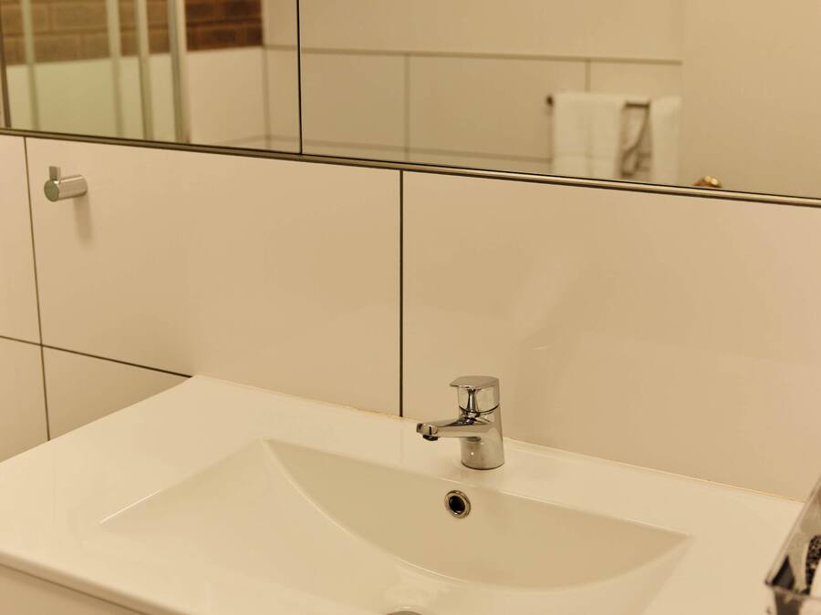 Un baño con un lavabo blanco, un espejo y un muro cubierto de azulejos.