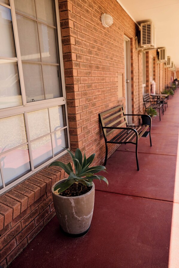A brick building with large windows, a potted plant, and outdoor seating.