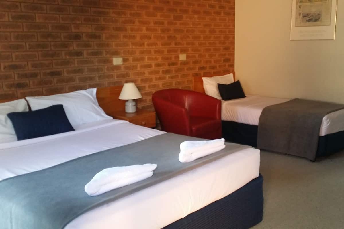 A hotel room with two beds, a red chair, and a lamp.