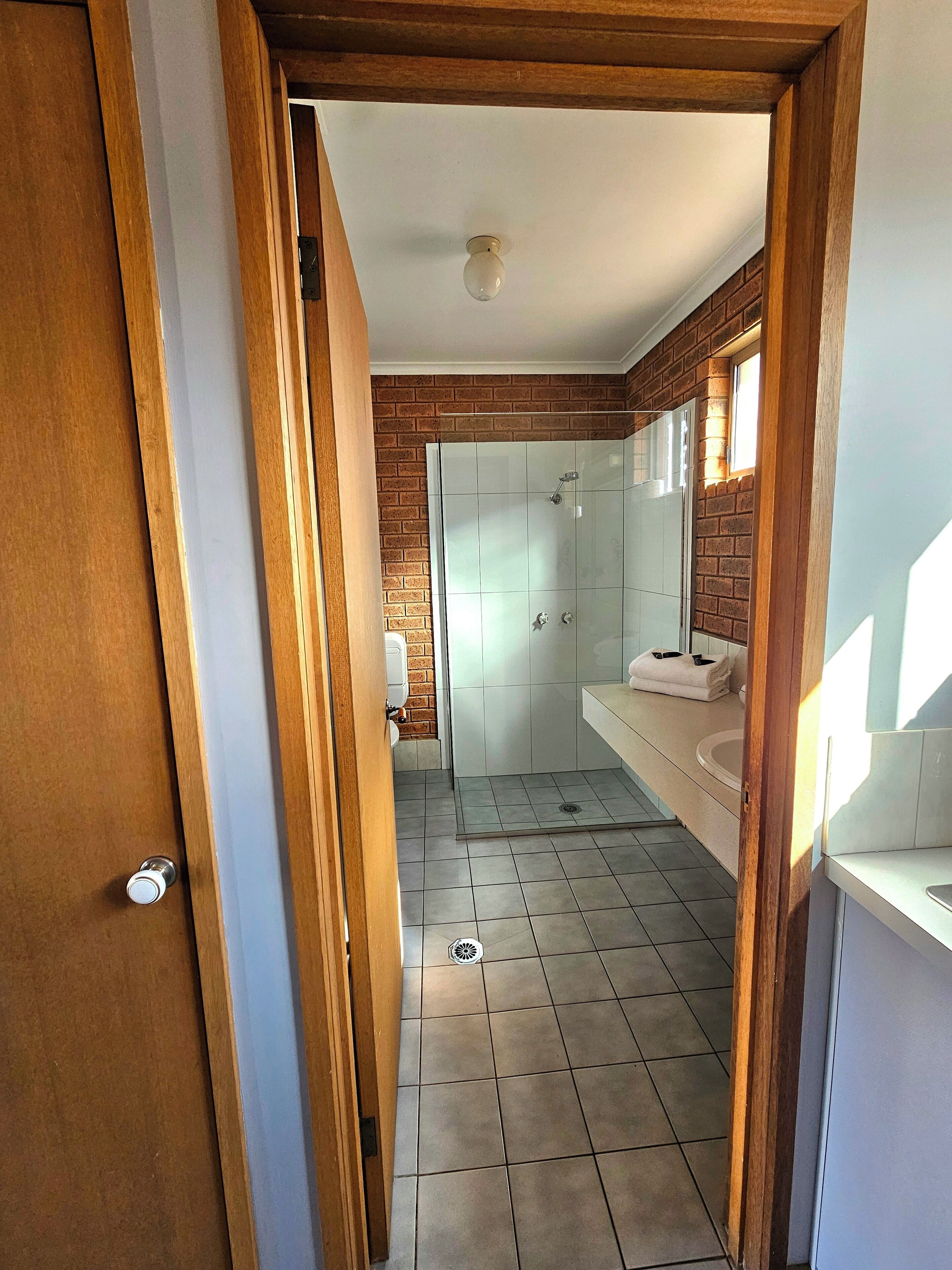 A narrow hallway leading to a bathroom with a shower, tiled floor, and a wooden door frame.