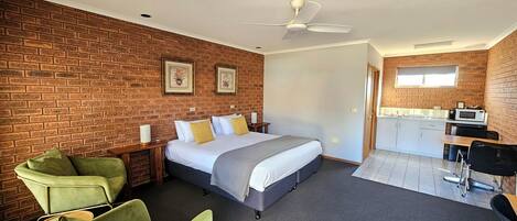 A hotel room with a brick wall, a bed, a desk, a chair, and a kitchenette.