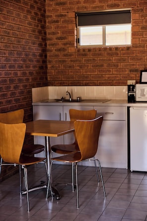 Une cuisine avec un mur en briques, une fenêtre, un évier, un four à micro-ondes et une table avec des chaises.