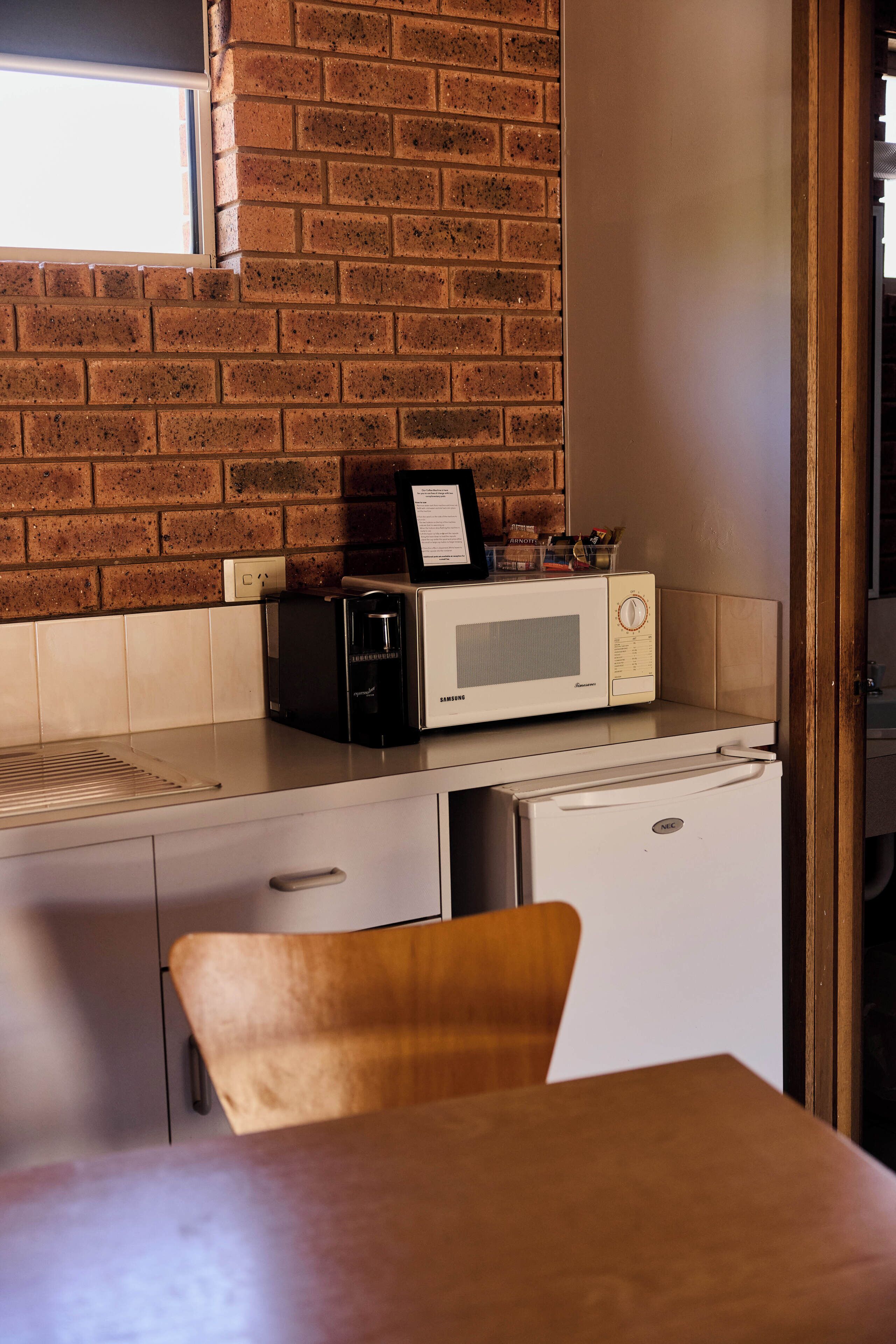 A compact kitchen with a microwave, a small refrigerator, and a wooden chair.
