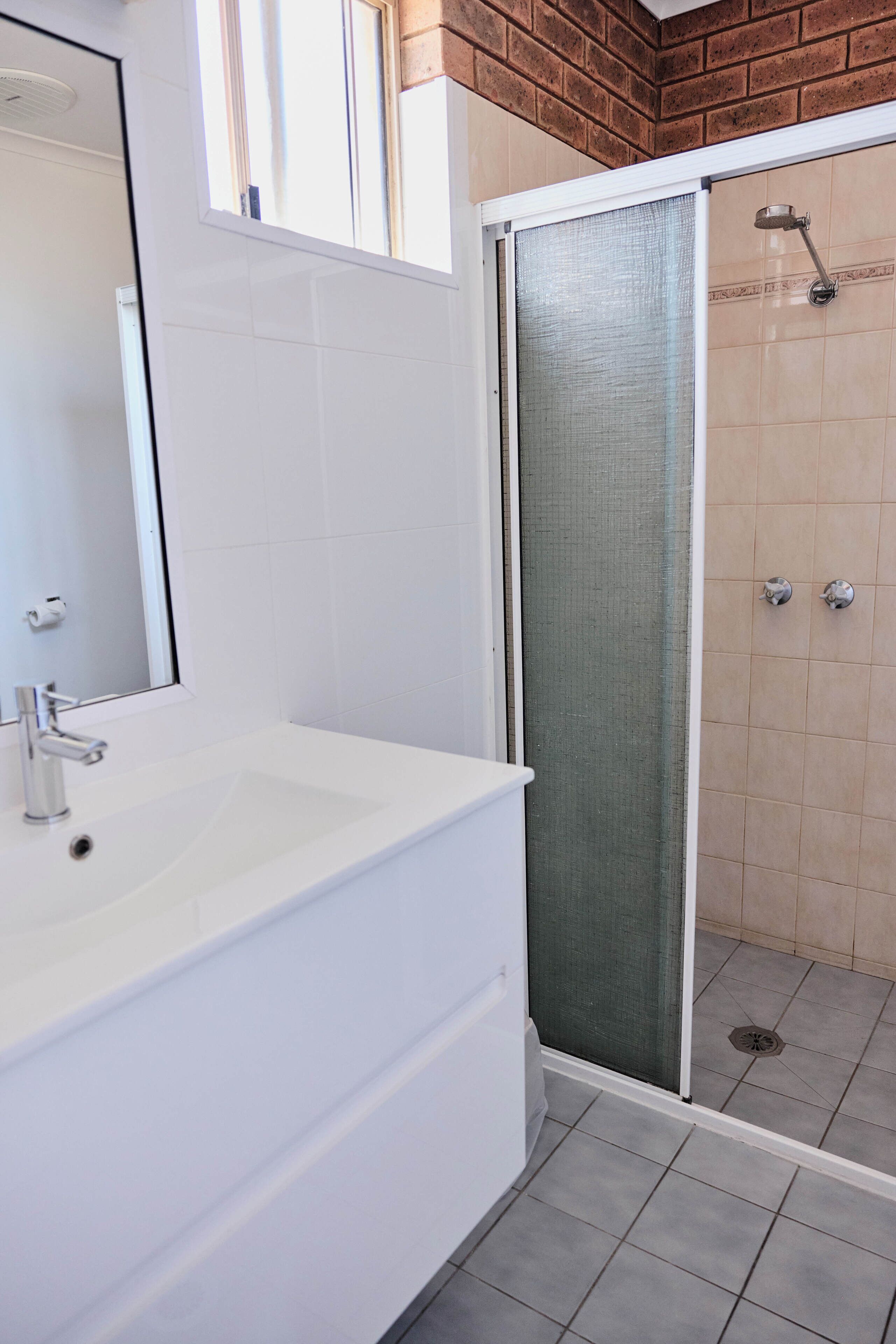 Une salle de bain avec un lavabo blanc, un miroir, une douche avec une porte en verre et un sol carrelé.