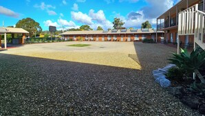 A motel with a gravel parking area, a covered waiting area, and a building with multiple rooms. - Bridge Motor Inn (Tocumwal)