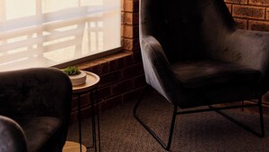 A room with a brick wall, a window with blinds, a round table with a plant, and two black chairs. - Bridge Motor Inn (Tocumwal)