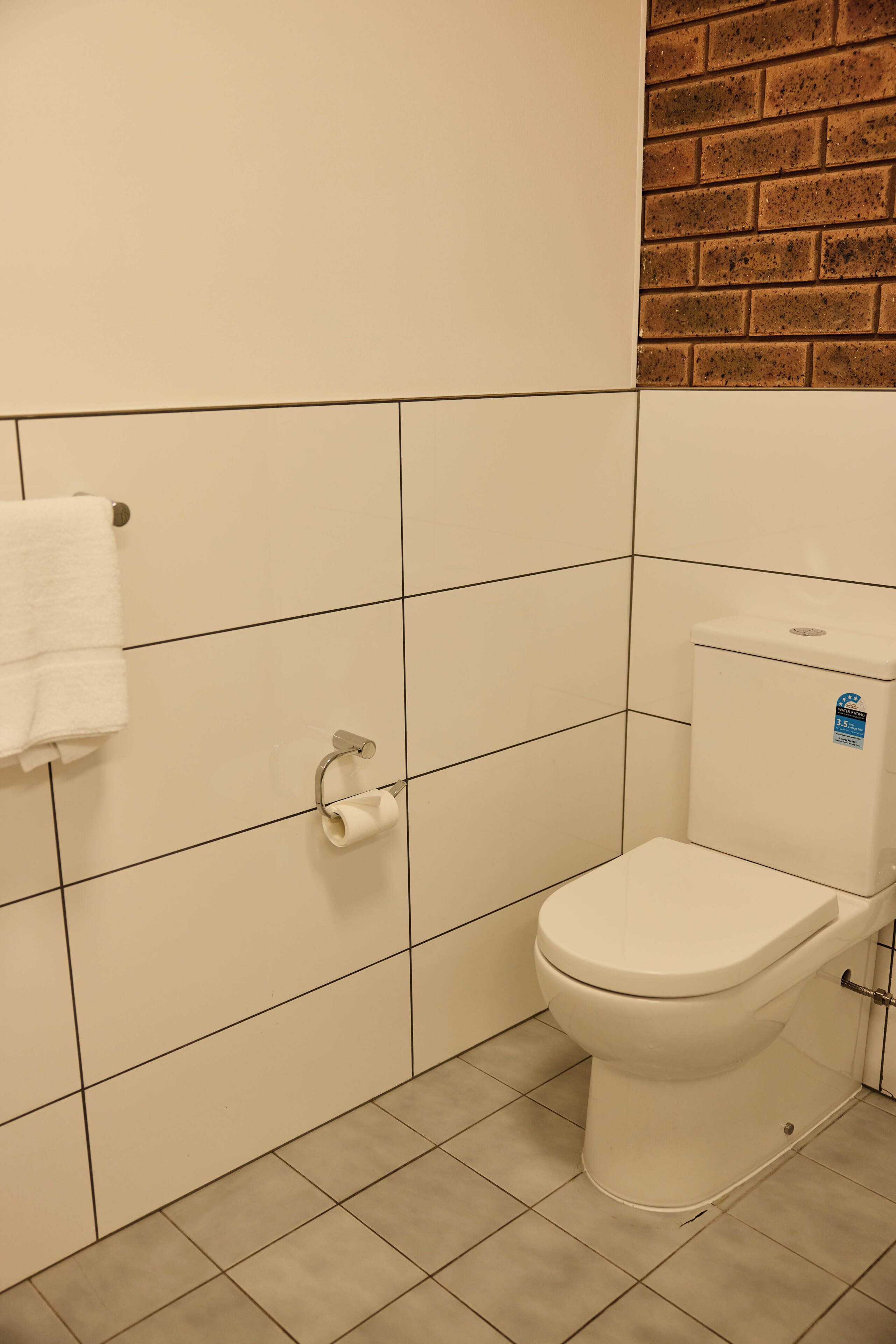 Een badkamer met witte betegelde wanden, een wit toilet en een handdoek aan een metalen haak.