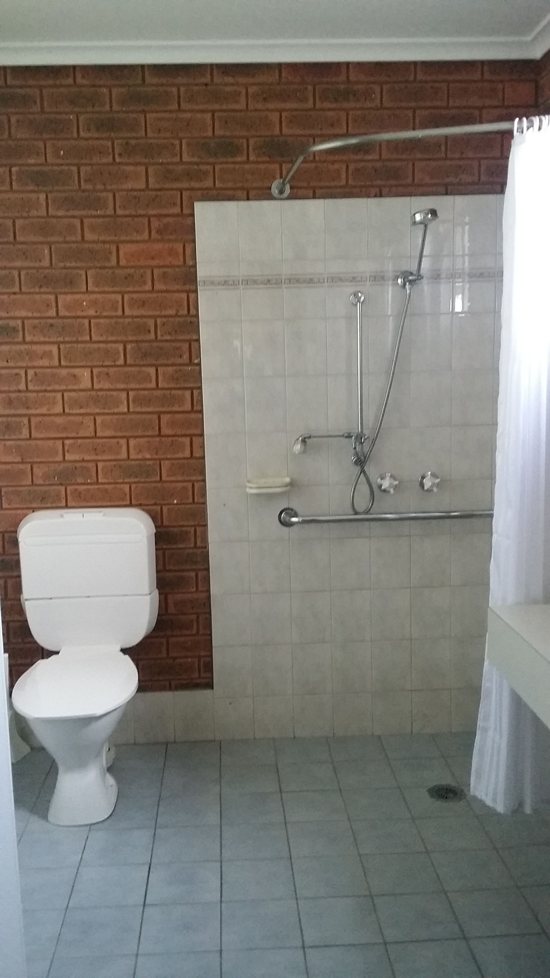 A bathroom with a white toilet, a shower with a glass door, and a tiled floor.