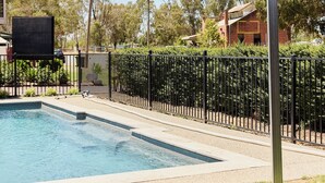 A swimming pool with a black metal fence, surrounded by grass and trees. - Bridge Motor Inn (Tocumwal)