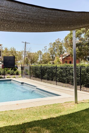 A swimming pool with a black metal fence, surrounded by grass and trees. - Bridge Motor Inn (Tocumwal)