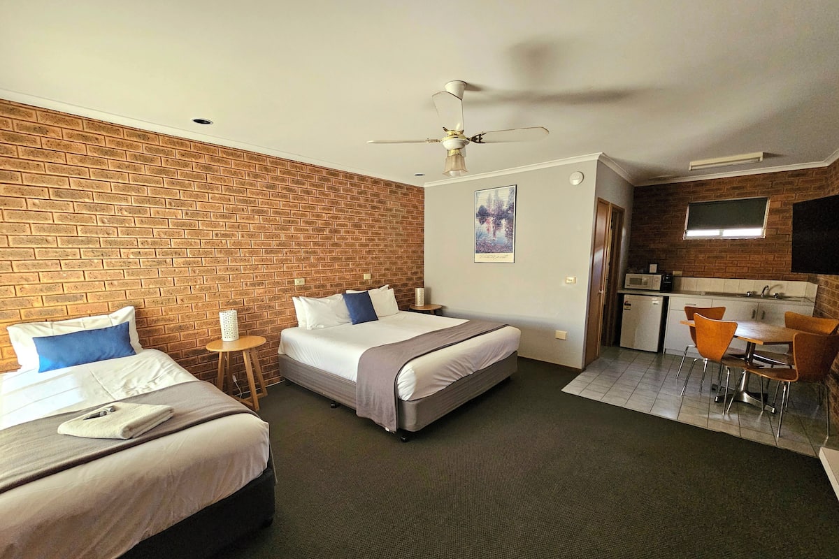 A hotel room with two beds, a kitchenette, and a dining area.