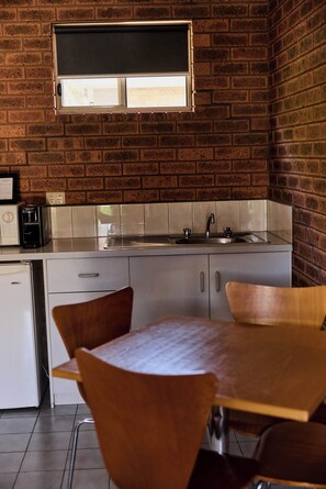 Une cuisine avec un mur en briques, une fenêtre au-dessus de l’évier, une machine à café et une table avec des chaises.