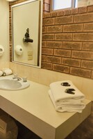 Un baño con lavamanos, espejo, toallero y pared de ladrillo.