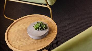 A green upholstered chair, a small round wooden table with a gray ceramic bowl and green plants, and a dark carpeted floor.