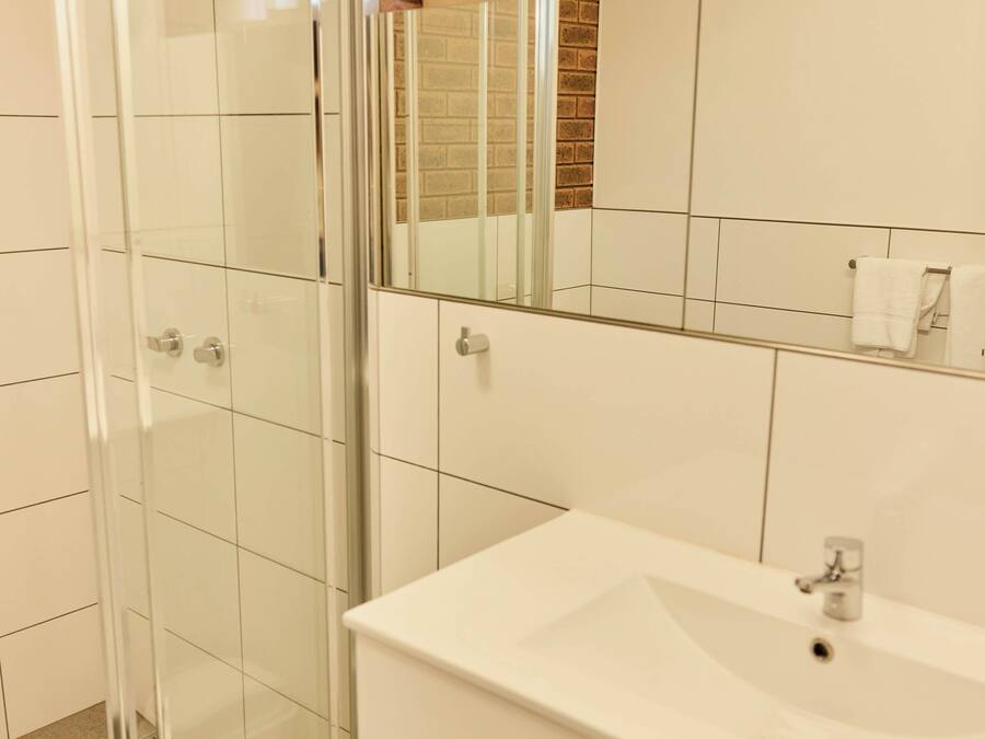 Un bagno con box doccia in vetro, un lavandino bianco e uno specchio sopra il lavandino.