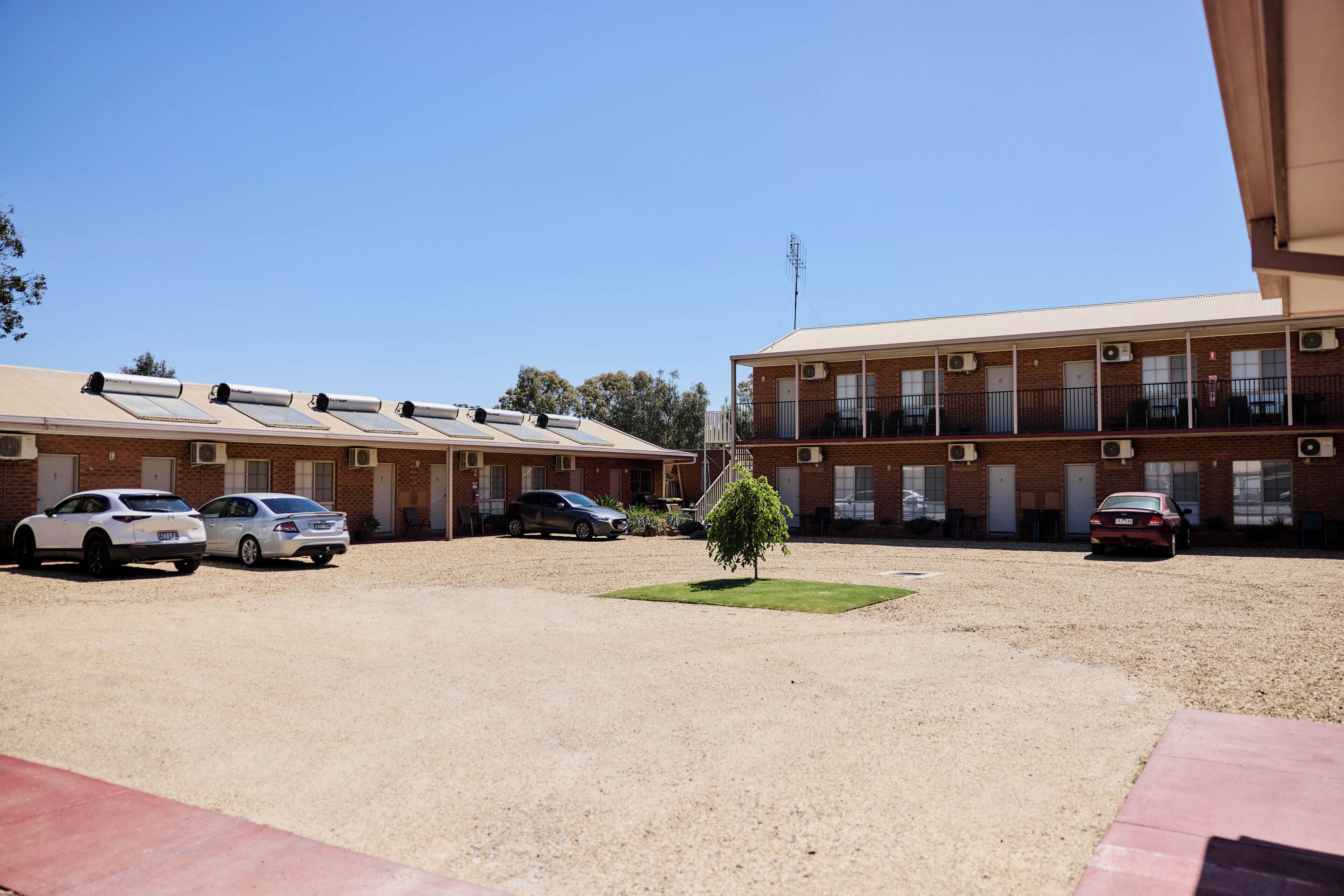 A motel with multiple rooms, a gravel parking area, and a small tree.