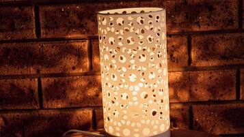 A cylindrical lamp with a perforated design on a round table against a brick wall.