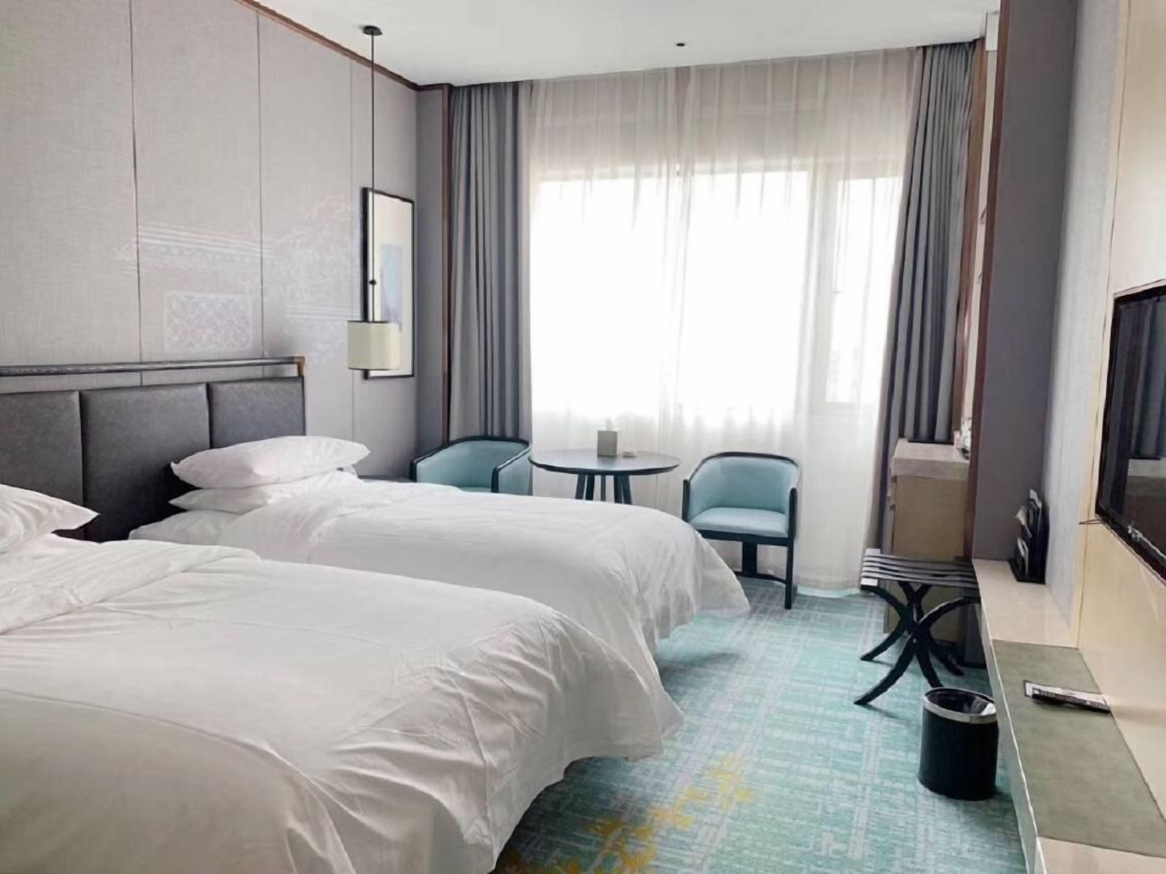 A hotel room with two beds, a small table, a chair, and a TV.