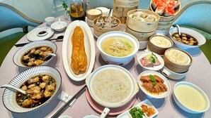 Ein runder Tisch mit verschiedenen Gerichten, darunter Knödel, Suppe und eine Auswahl an Beilagen, in einem modernen Innenraum mit Glasgeländer im Hintergrund.