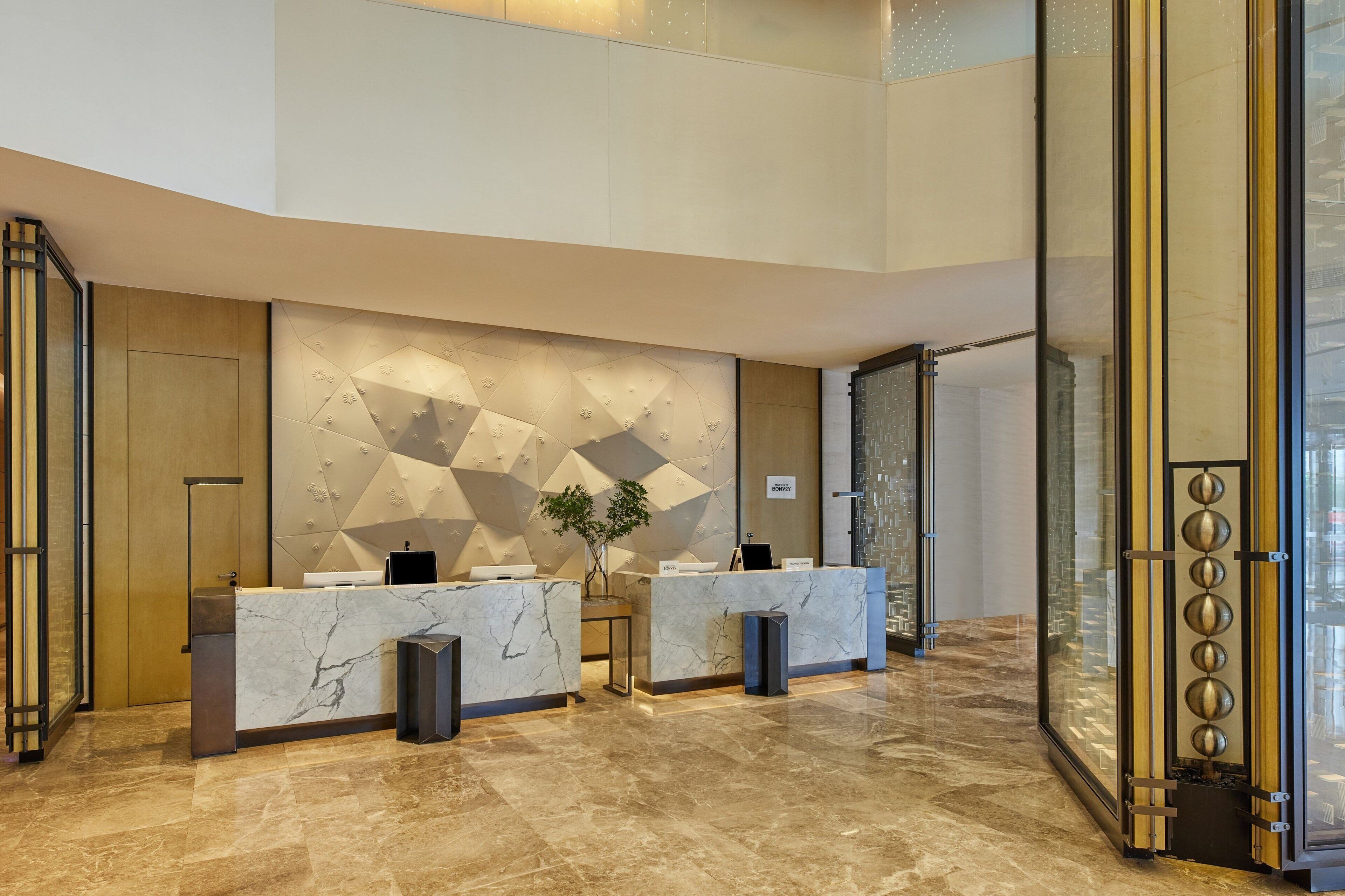 A modern reception area with marble counters, a geometric wall design, and a glass door leading to a balcony.