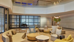 Eine geräumige Lobby mit einer gebogenen Couch, runden Couchtischen und einem Flügel.