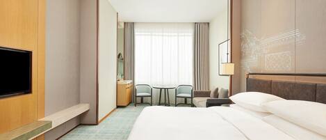 A hotel room with a large bed, a TV, a desk with a chair, and a small table.