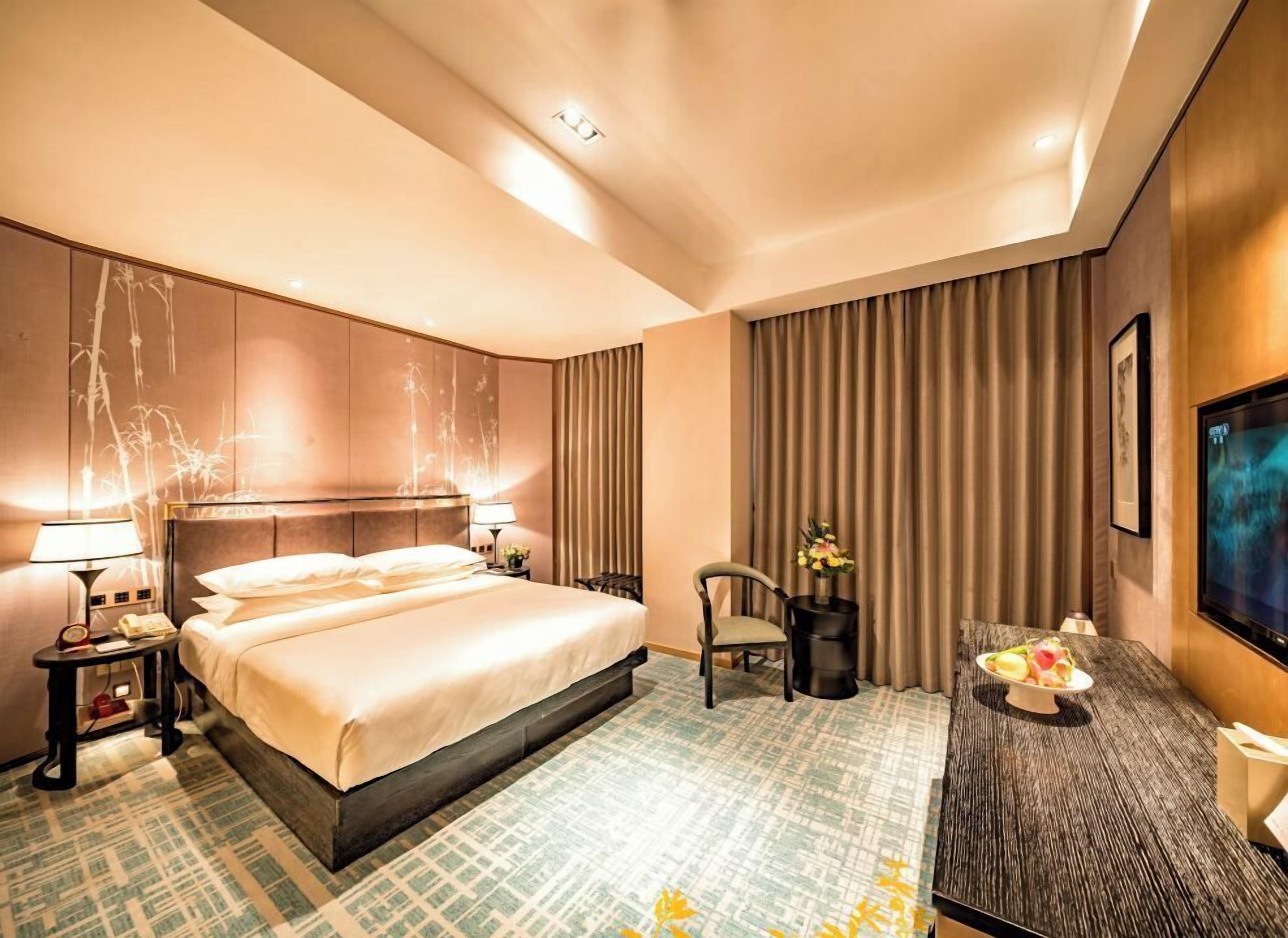 A hotel room with a large bed, a desk, a chair, and a television.
