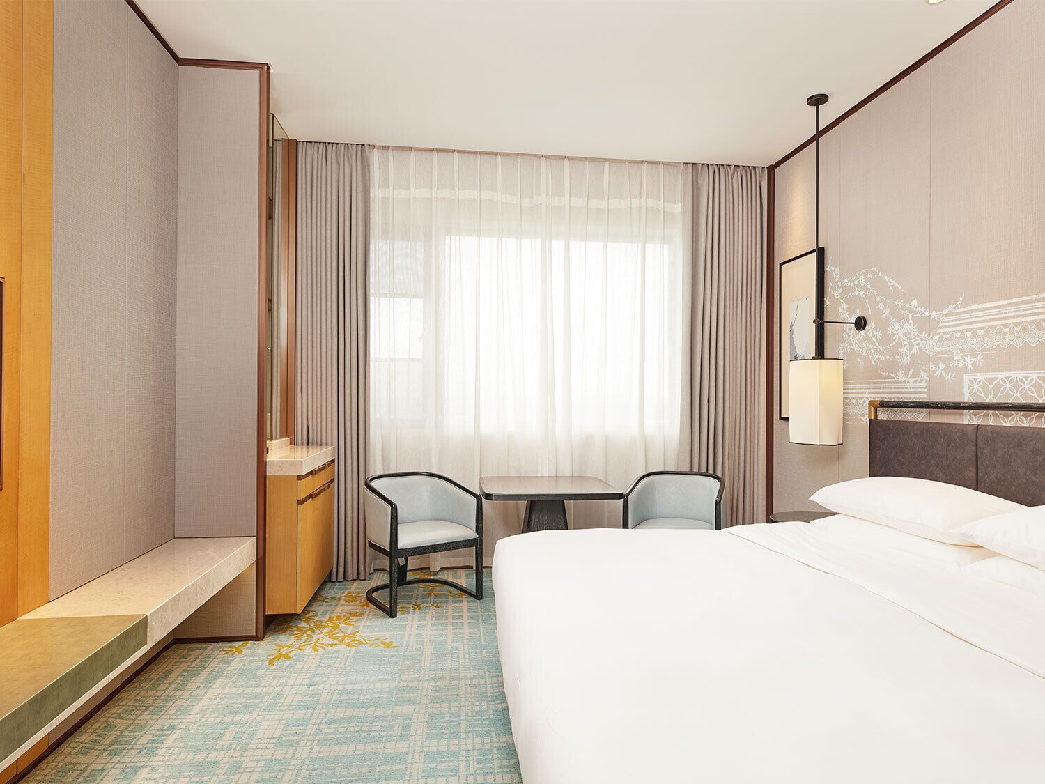 Hotelkamer met een bed, een bureau, twee stoelen, een kleine tafel, een spiegel en een wandlamp.