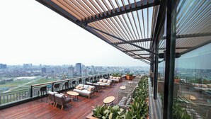 Eine Dachterrasse mit Holzboden, Sitzgelegenheiten im Freien und Blick auf die Stadt.