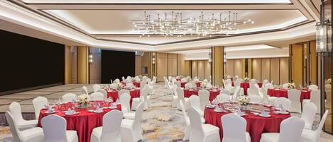 A banquet hall with round tables set for dining, white chairs, and a central chandelier.