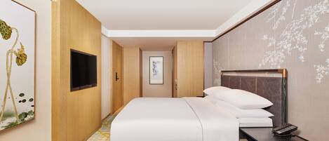 A hotel room with a bed, a TV, a bedside table, and a framed picture on the wall.