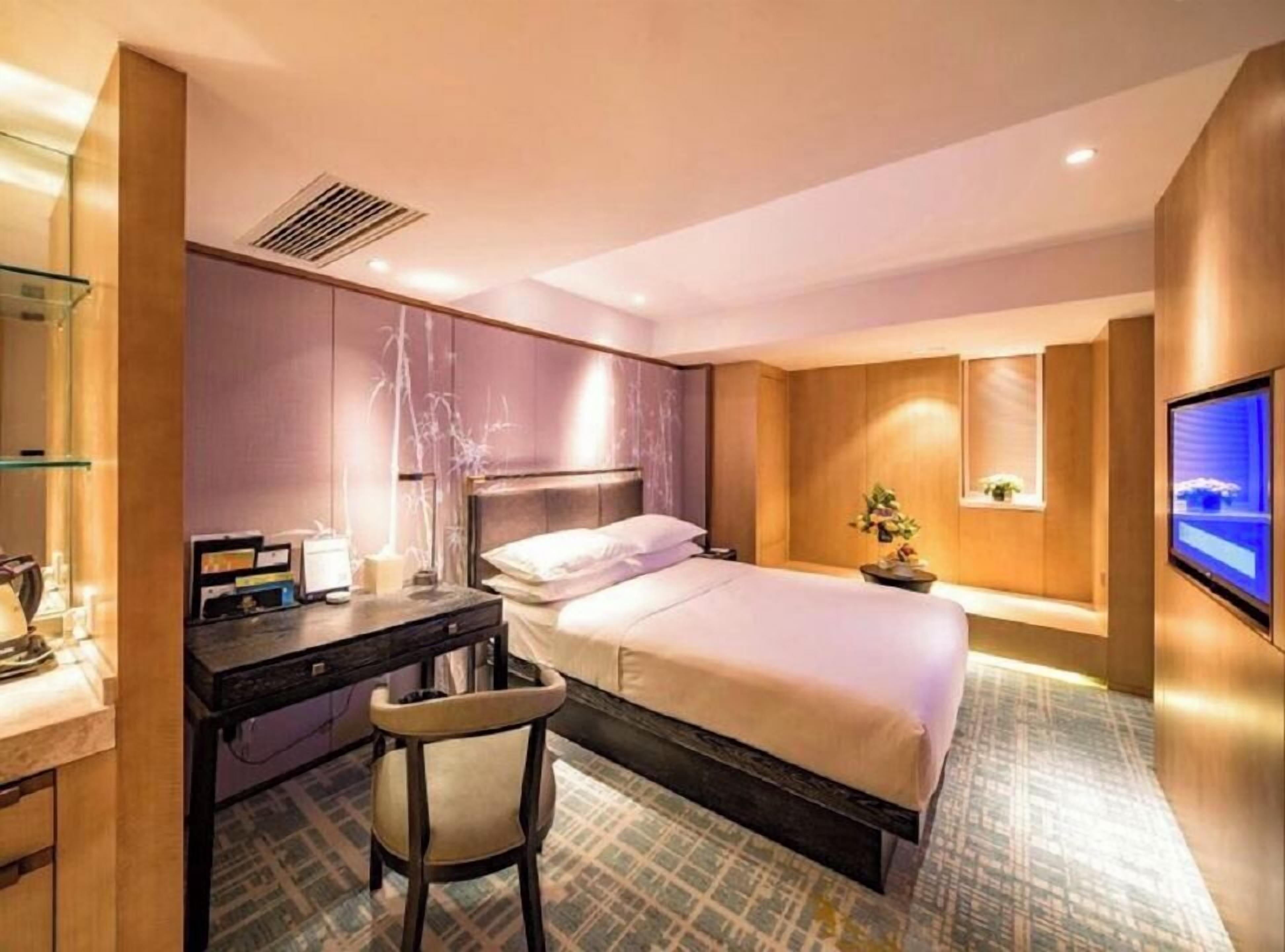 A modern hotel room with a bed, desk, chair, and a television on the wall.