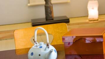 A table with a white teapot with blue patterns, a plate with food, and a framed picture of a mountain on the wall.