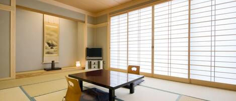 A traditional Japanese room with tatami flooring, a low table, a television, and sliding doors.