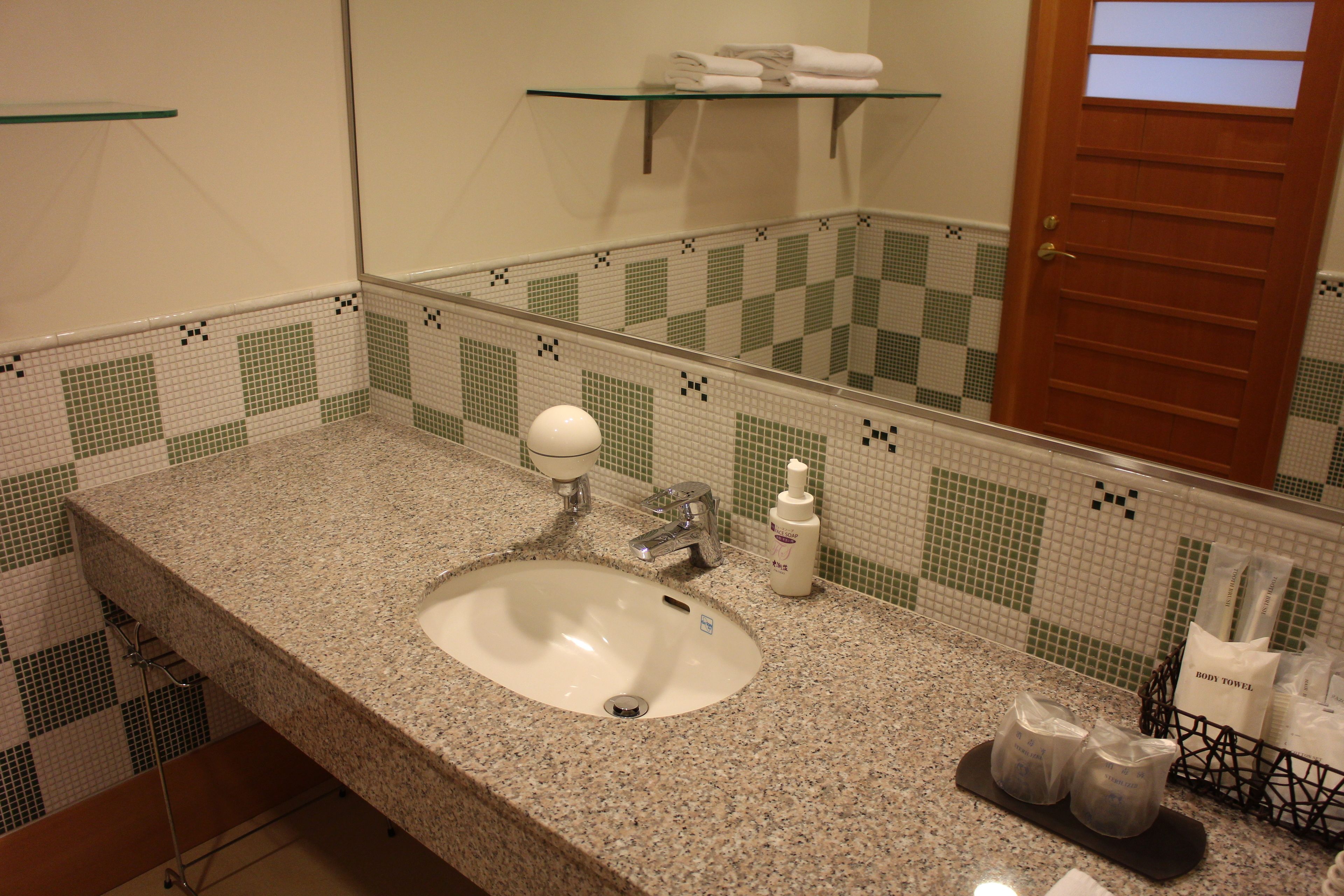 Une salle de bain avec un lavabo doté d’un plan de travail en granit, un miroir, un porte-serviettes et un espace douche.