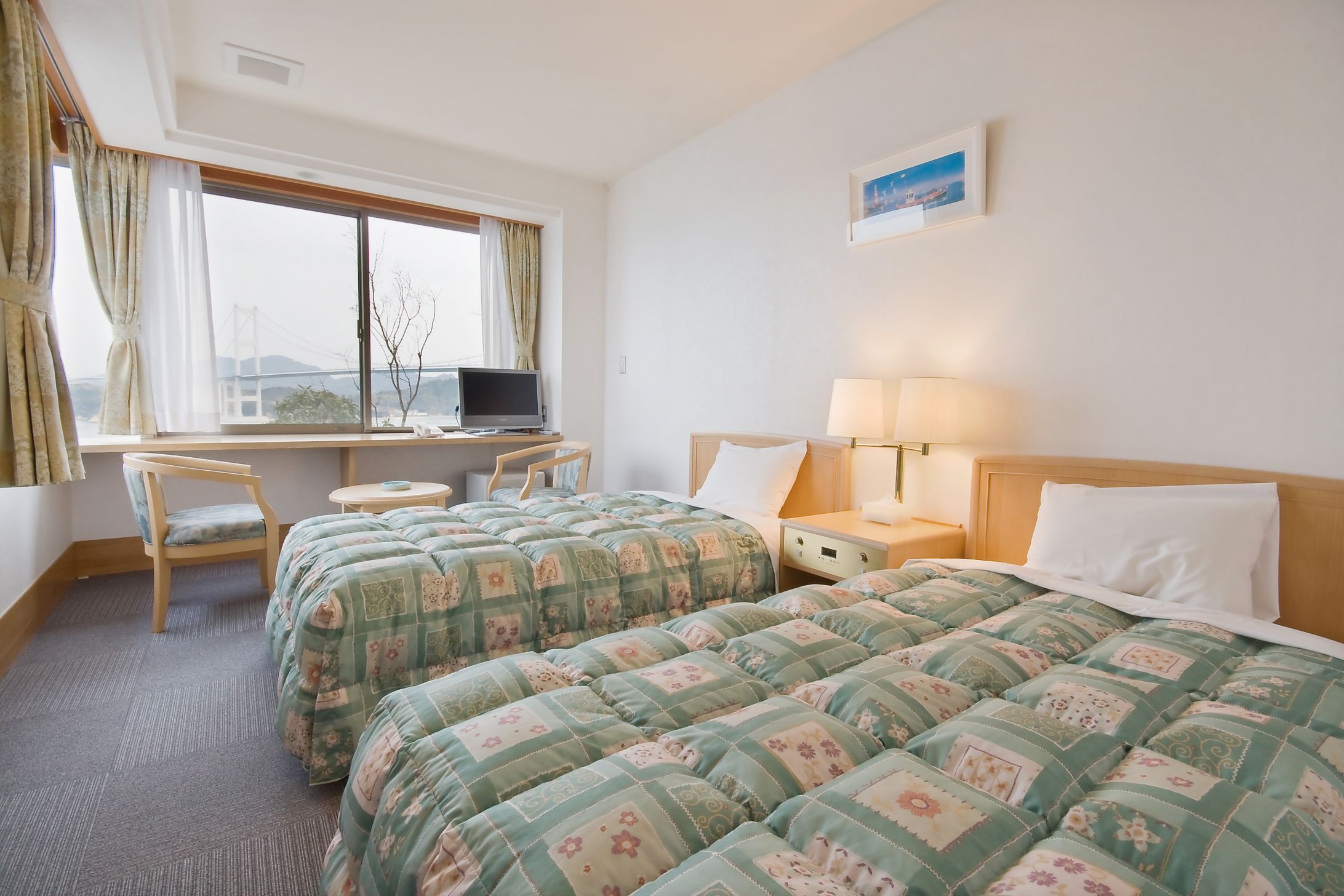 A hotel room with two beds, a desk, a chair, a lamp, and a window with curtains.
