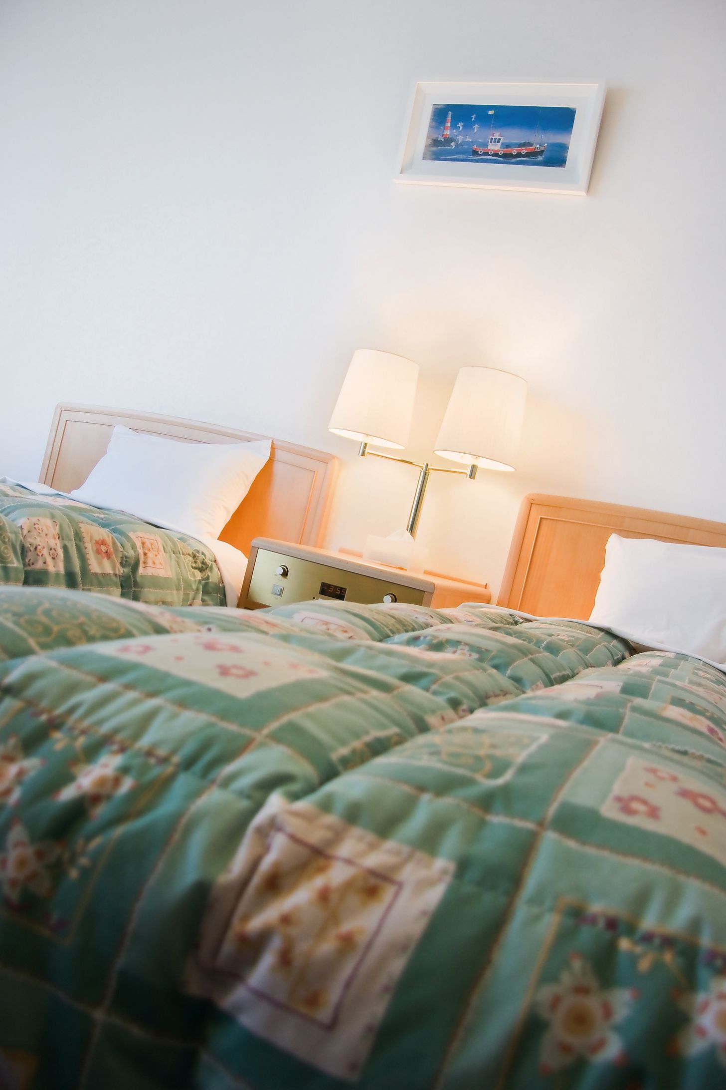 A hotel room with two beds, each with floral-patterned bedding, a nightstand with lamps, and a framed picture on the wall.