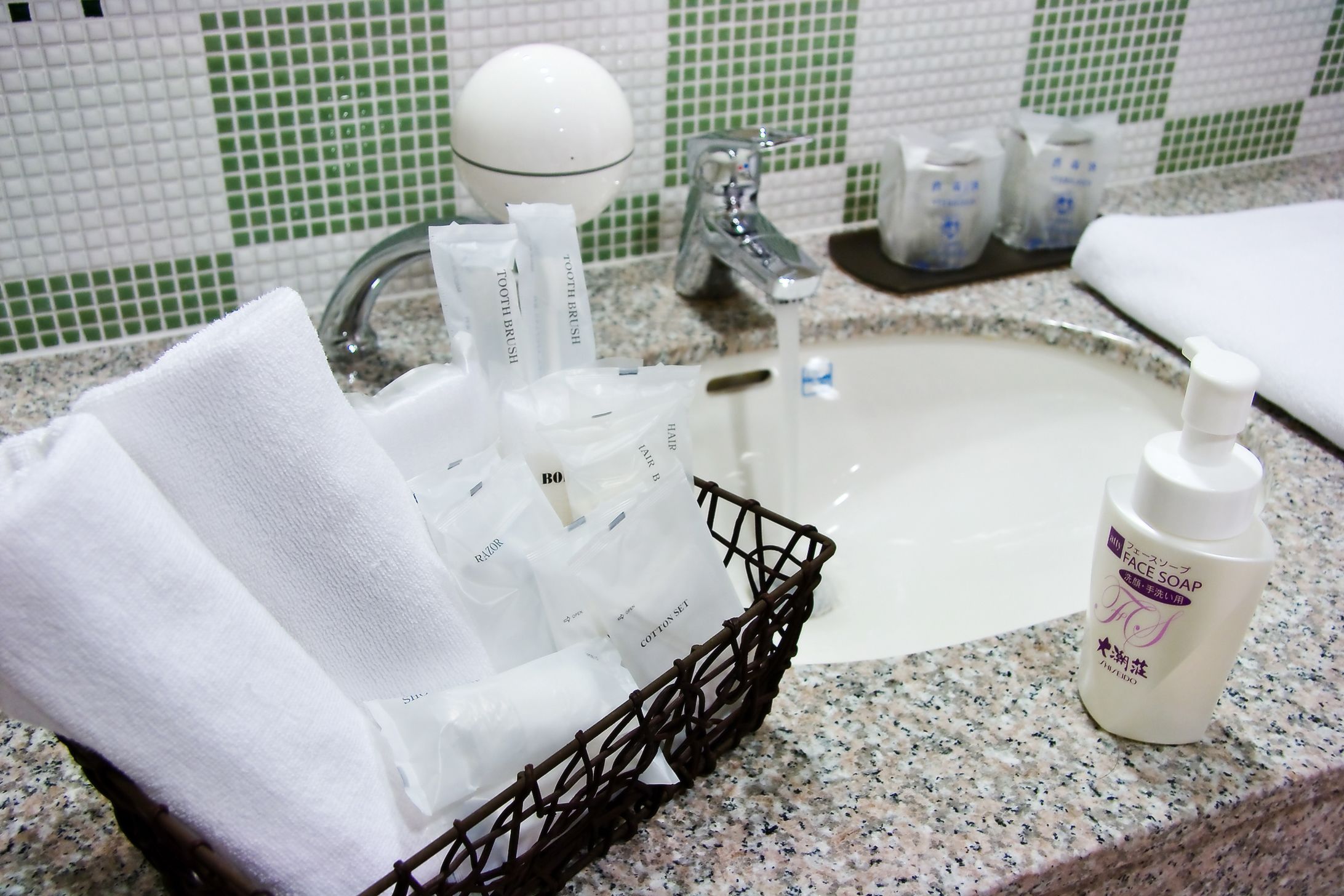 A bathroom sink with toiletries, a bottle of face soap, and a basket of towels.