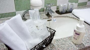 Un lavamanos de baño con artículos de aseo, una botella de jabón facial y una cesta de toallas.