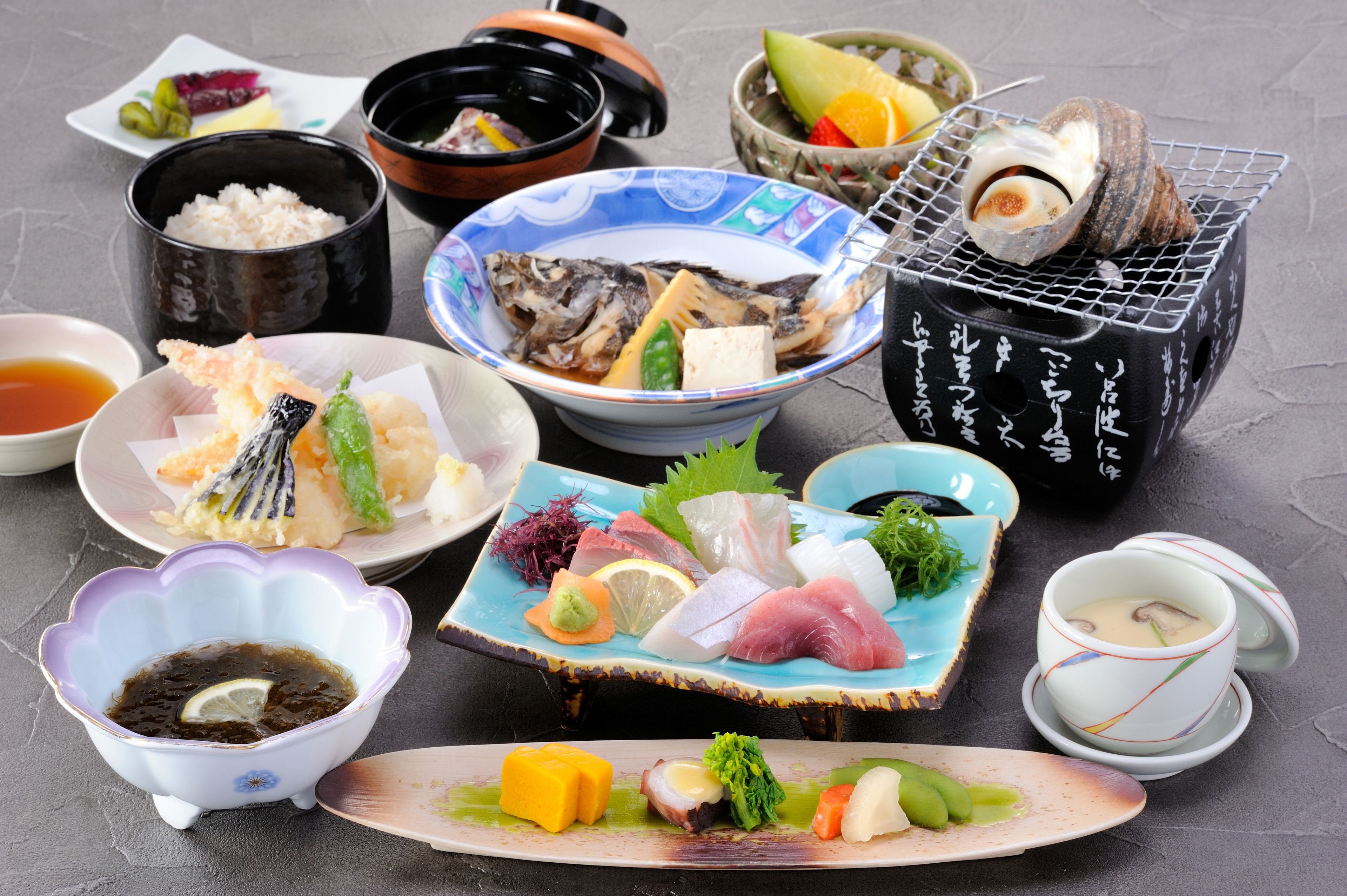 Variedad de platos japoneses, como sushi, sashimi y tempura, servidos en distintos platos y tazones.