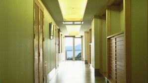 A long, narrow hallway with wooden doors on both sides, leading to a bright room with a view of the outdoors. - Daichoso (Imabari)