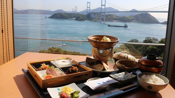 A table with a variety of dishes and a view of a bridge over water. - Daichoso (Imabari)